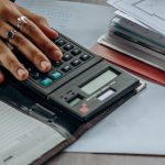 Mano su una calcolatrice accanto a documenti per il calcolo del reddito imponibile nel regime forfettario