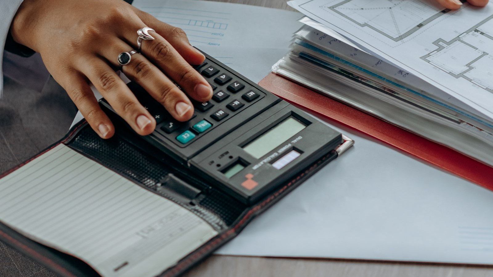 Mano su una calcolatrice accanto a documenti per il calcolo del reddito imponibile nel regime forfettario